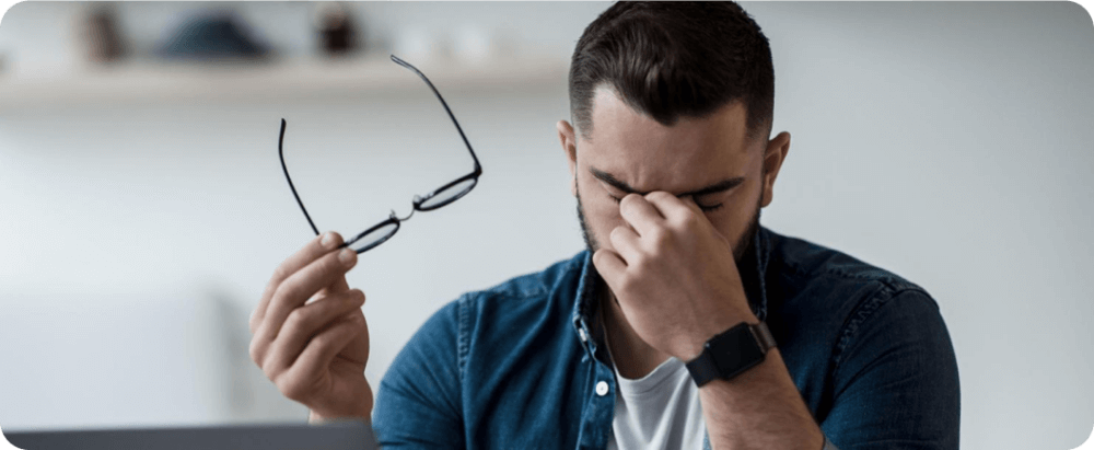 A man taking off his glasses and holding his face