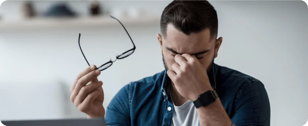 A man taking off his glasses and holding his face
